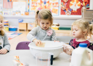 Two preschool girls using a mixing bowl to cook
