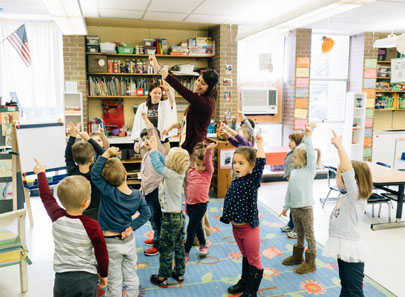 Preschool children and teacher in a classroom all pointing upwards