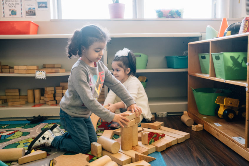 Two children playing a blocks on a classroom floor. One child looks away as the other builds a tower.