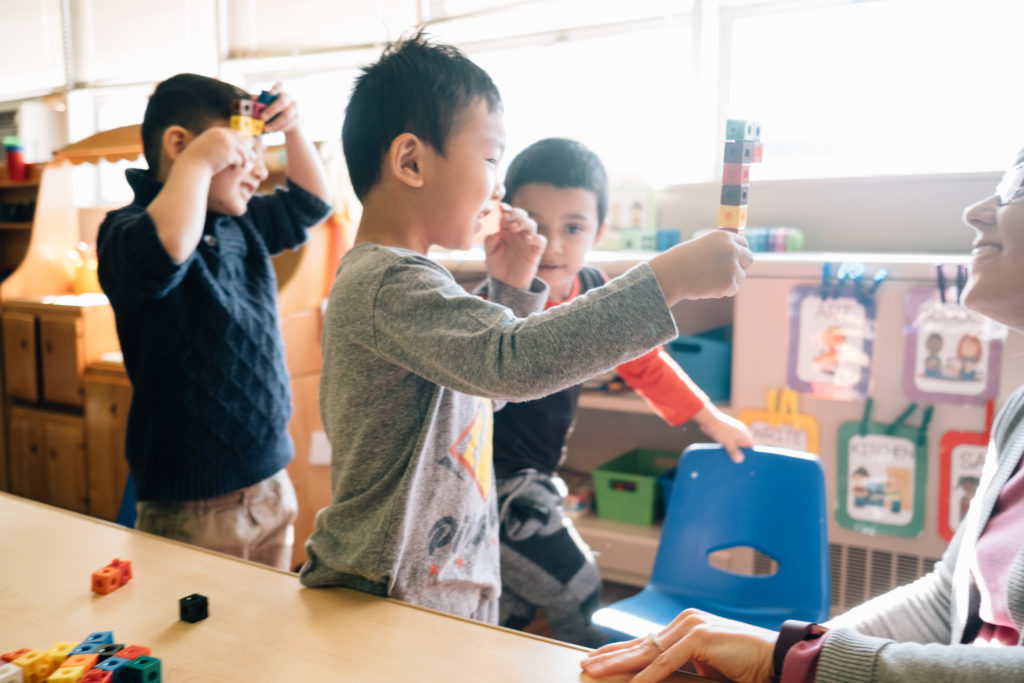 Three young children stand together, moving their hands about in the air.