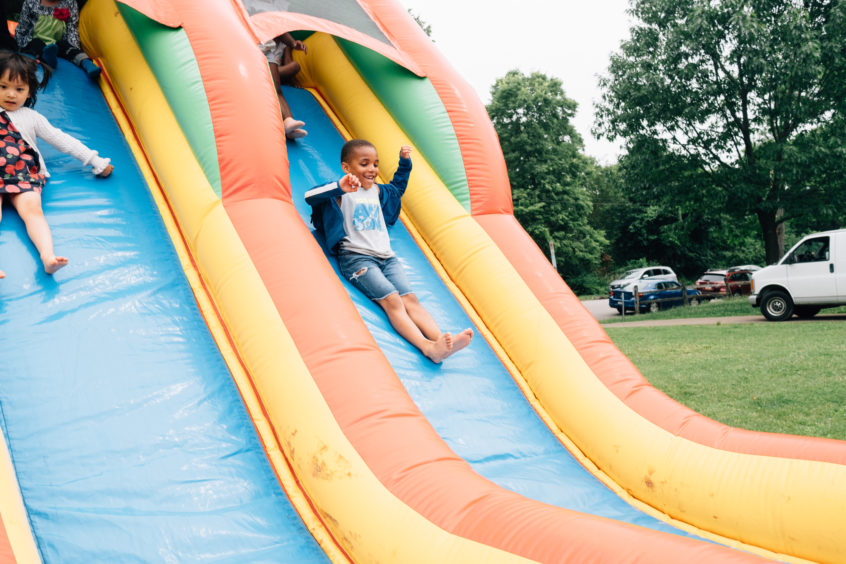 Picture: Several children slide down a bouncy slide with wide grins and their hands raised.
