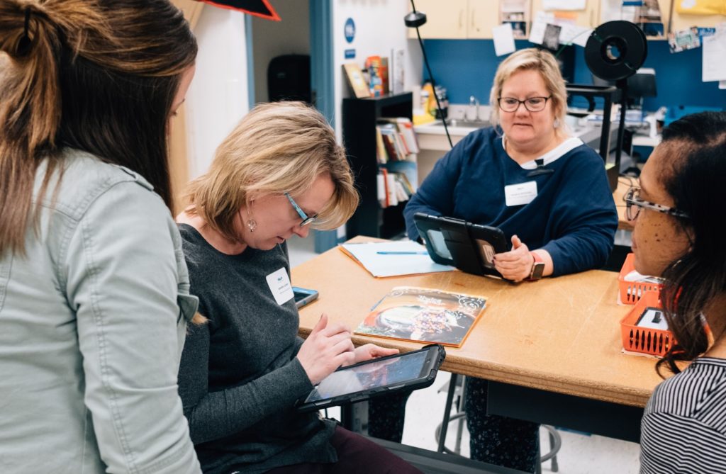 At a table, early childhood professionals sit together while reviewing material on a digital device.