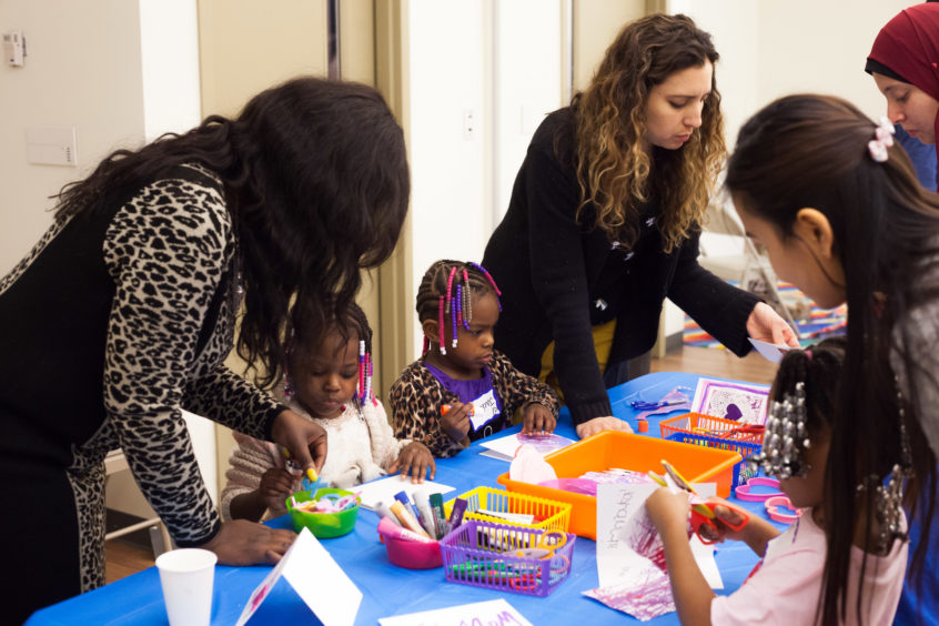 Image: Young children and adults gather together to participate in a fun table activity.