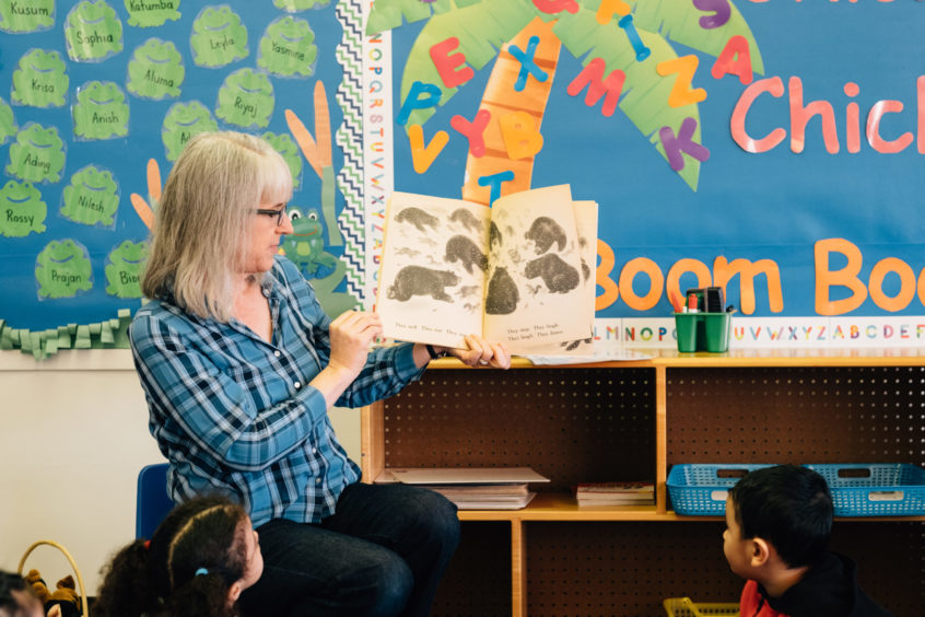 Image: An early childhood professional holds a picture book up for the children, reading along together with them.