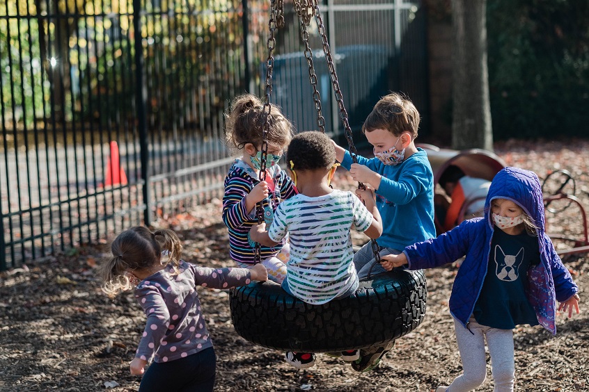 Image: Five young children play together on a tire swing at a local child care program.