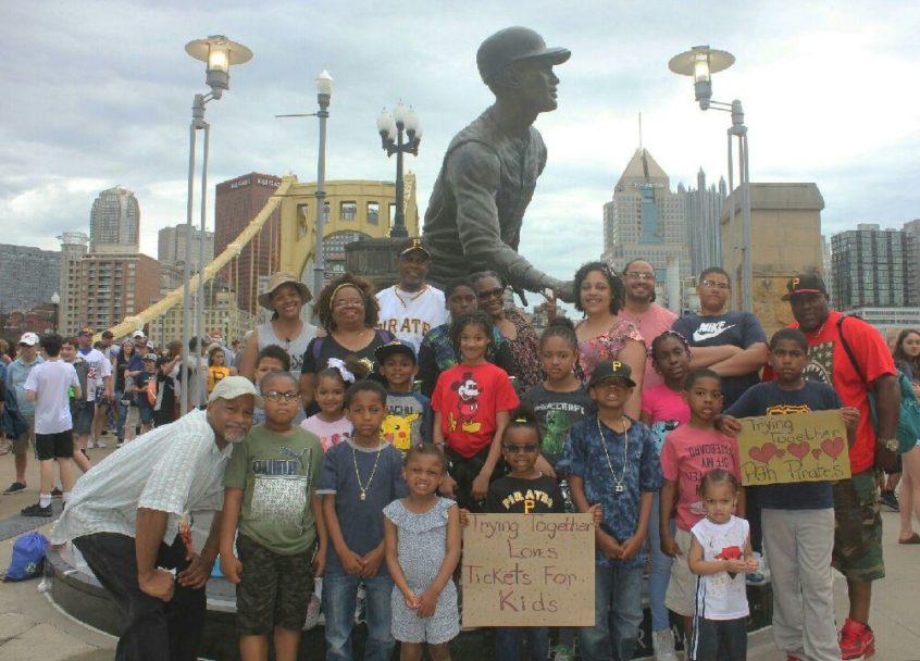Image: Several families from Homewood join together in front of a statue by PNC Park, smiling together joyfully.