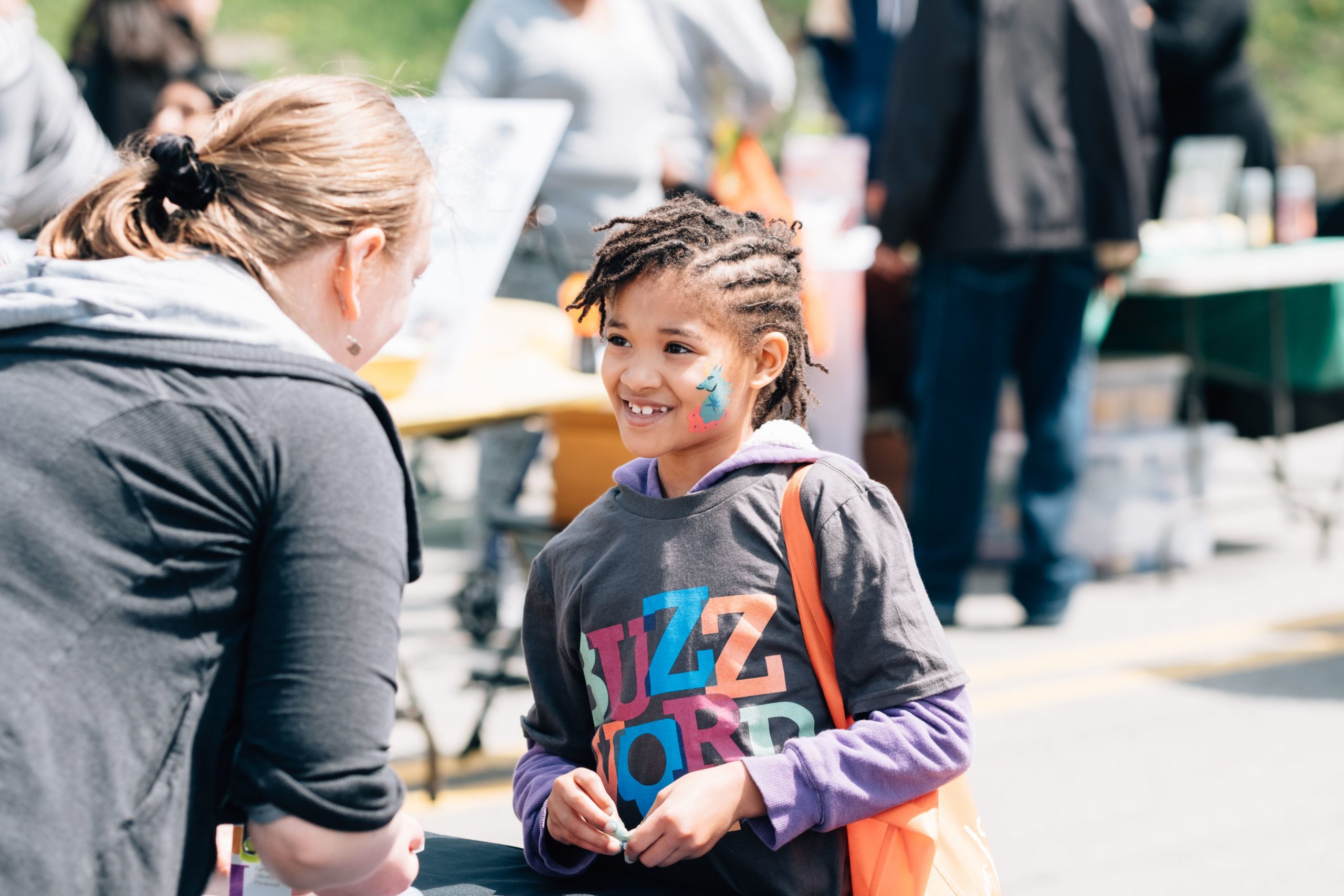 elementary aged young girl with face paint smiles and talks to a volunteer at an event