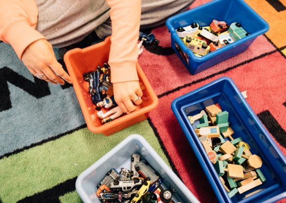 Image: An early learning professional sorts colorful toy pieces into four small boxes on the floor.