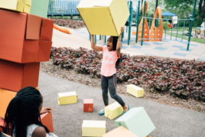 Girl on playground plays with block while smiling