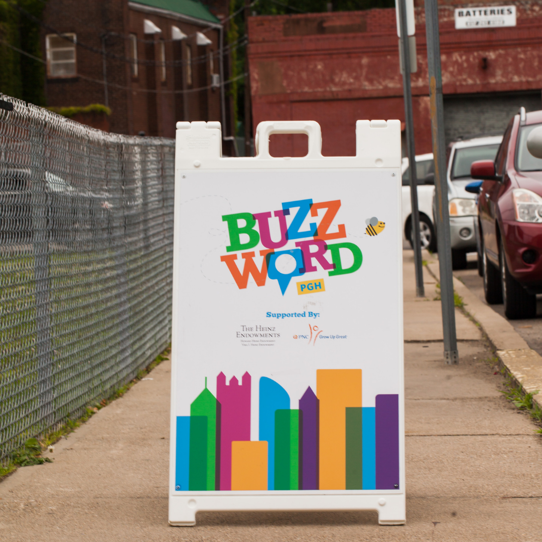 a sign displaying the Buzzword logo is displayed on the sidewalk next to a fence