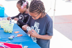 Two young children participate in a craft at an outdoor fair