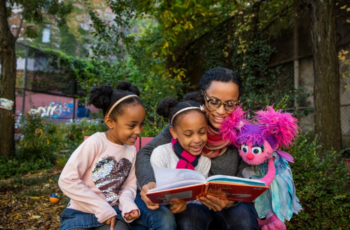 Adult reading to children with Sesame Street character.