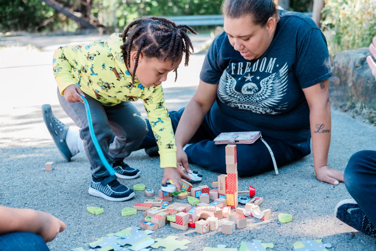 A young boy reaching down and playing with blocks while his mom sits close by | How Block Play Contributes to Spatial and Mathematical Skills