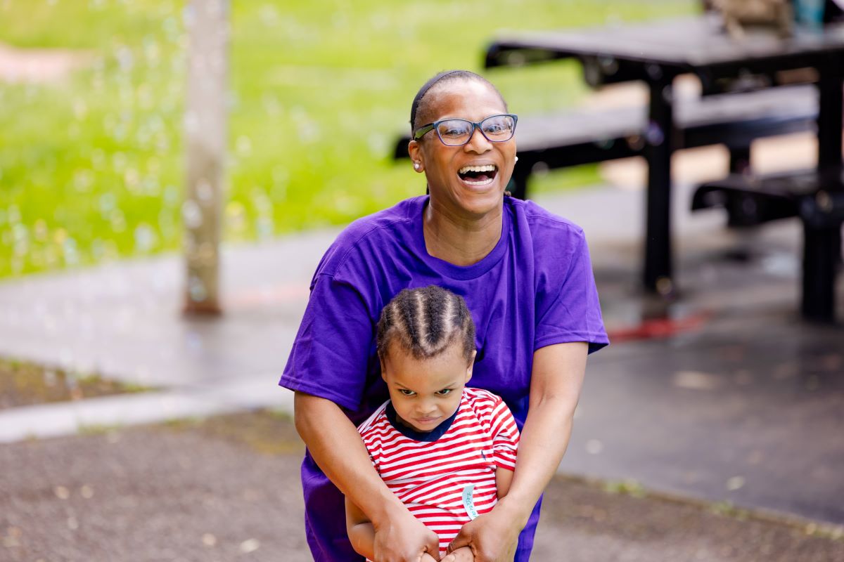 A woman smiling wrapping her arms around a child | Multigenerational Play Creates Intergenerational Impacts