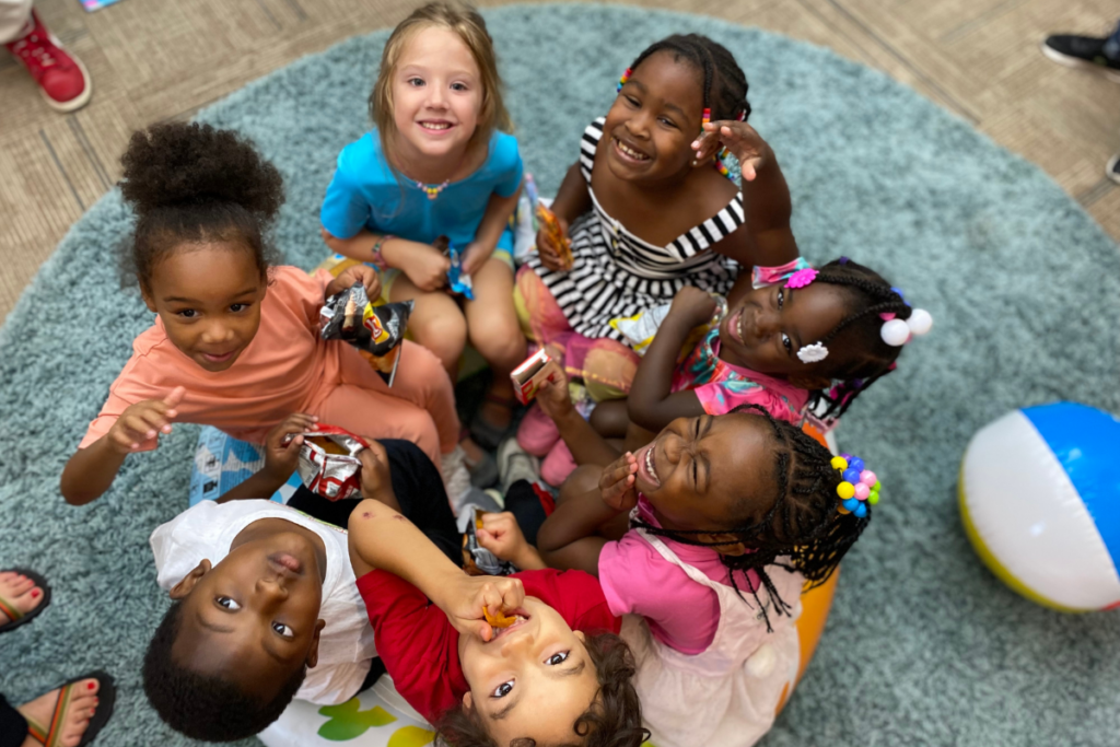 Children sitting in a group smiling up at the camera | The Role of Play in Child Development and Learning