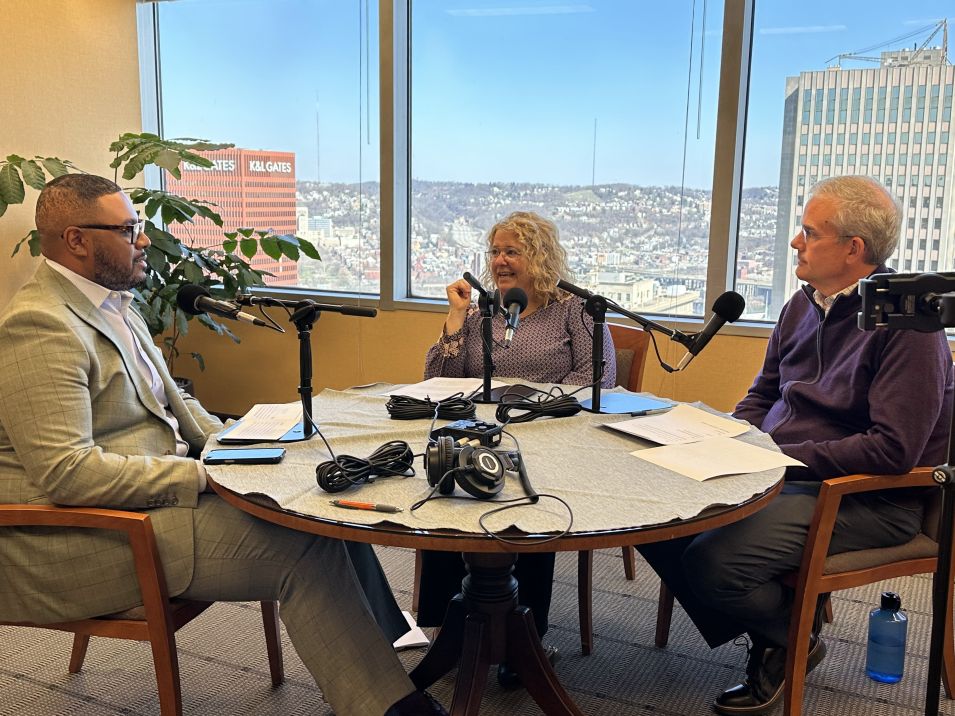 Two men and one woman sitting at a table recording a podcast