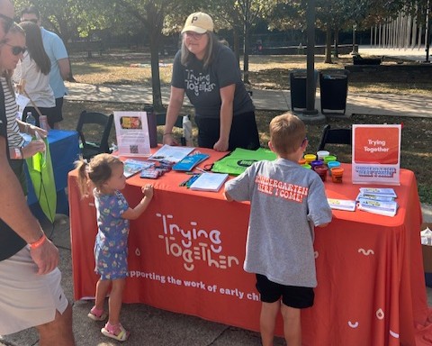 An adult stands behind a table talking to two children