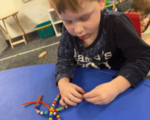 Young child playing sitting at a table playing with lacing beads