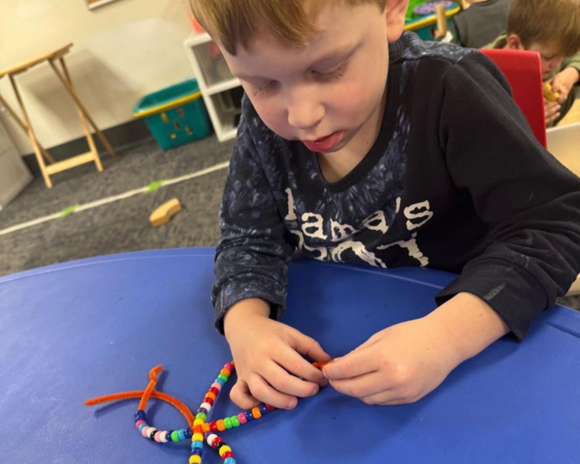 Young child playing sitting at a table playing with lacing beads